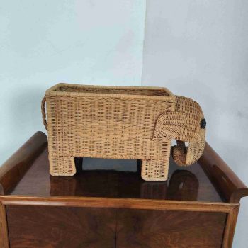 Porta riviste italiano in rattan intrecciato, a forma di elefante, su mobile vintage in legno, anni ’70.